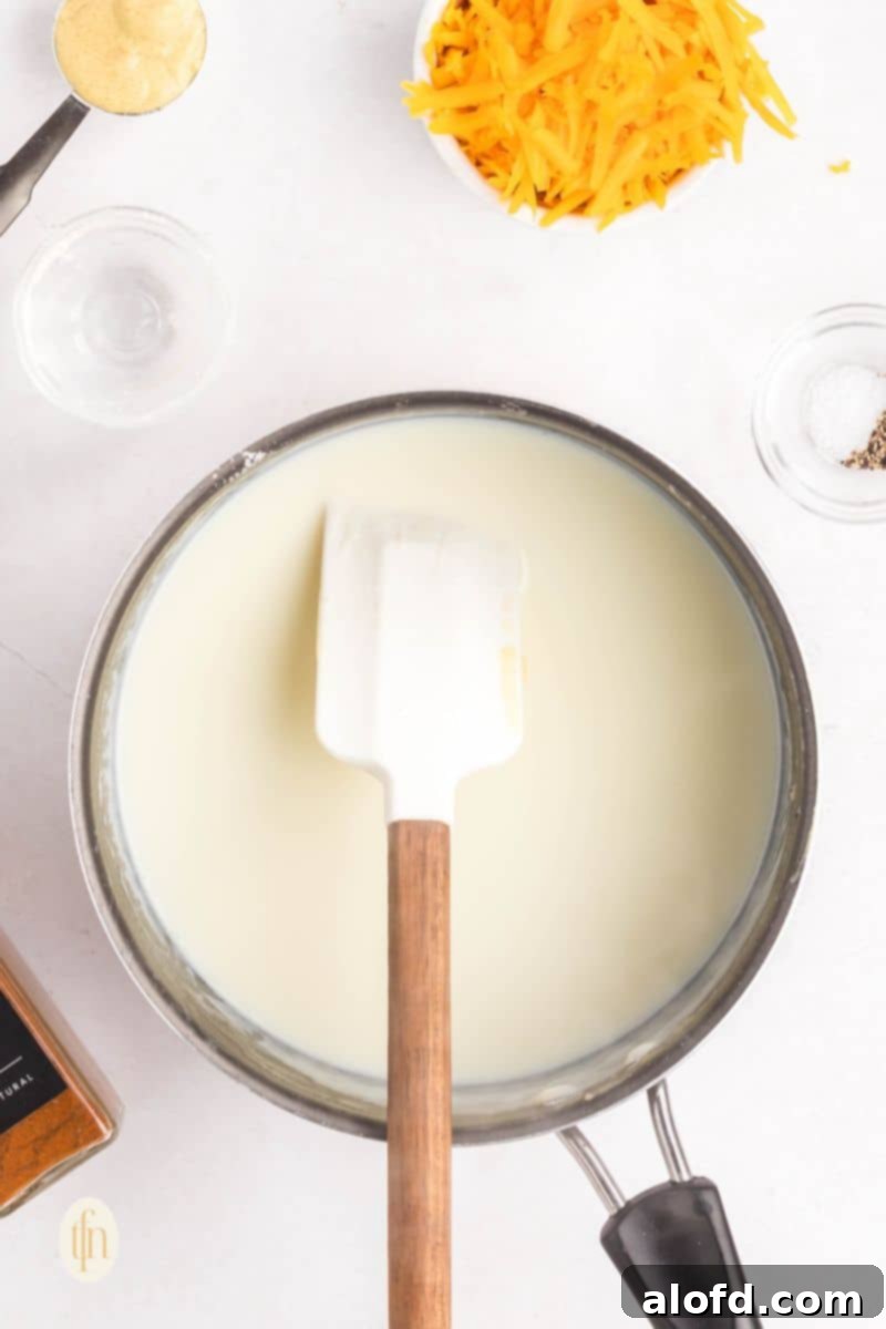 Loaded Pigs in a Blanket Bake 11 White sauce in a pan with ladle.