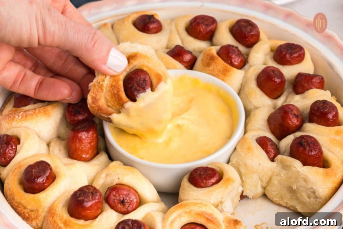 Loaded Pigs in a Blanket Bake 15 Dipped wrapped sausages with a bowl of sauce in the middle of the baking dish.