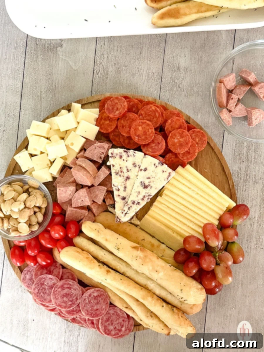Effortless Charcuterie Boards 11 A fully assembled round charcuterie board, abundant with a variety of meats, cheeses, garlic herb breadsticks, cherry tomatoes, grapes, and nuts, garnished with fresh rosemary.