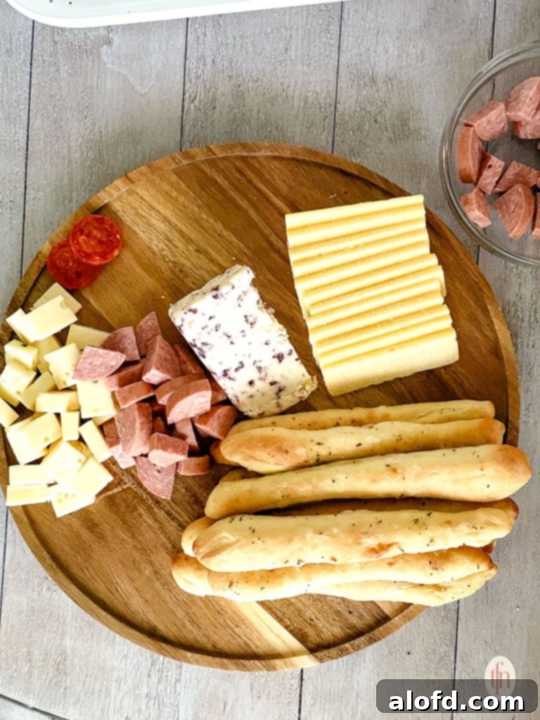 Effortless Charcuterie Boards 9 An initial stage of charcuterie board assembly, featuring breadsticks, sliced cheese, and folded meats arranged on a round wooden board.
