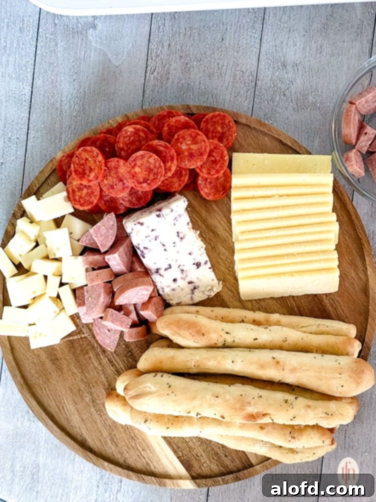 Effortless Charcuterie Boards 10 A charcuterie board further along in assembly, with more cheese varieties, meats, and the addition of cherry tomatoes and grapes, showcasing a colorful spread.