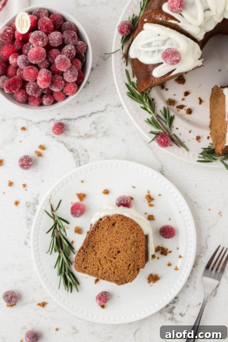 Spiced Molasses Bundt Cake 3 A perfectly sliced portion of gingerbread bundt cake on a pristine white plate, with the remainder of the glazed bundt cake and holiday decorations visible in the background.