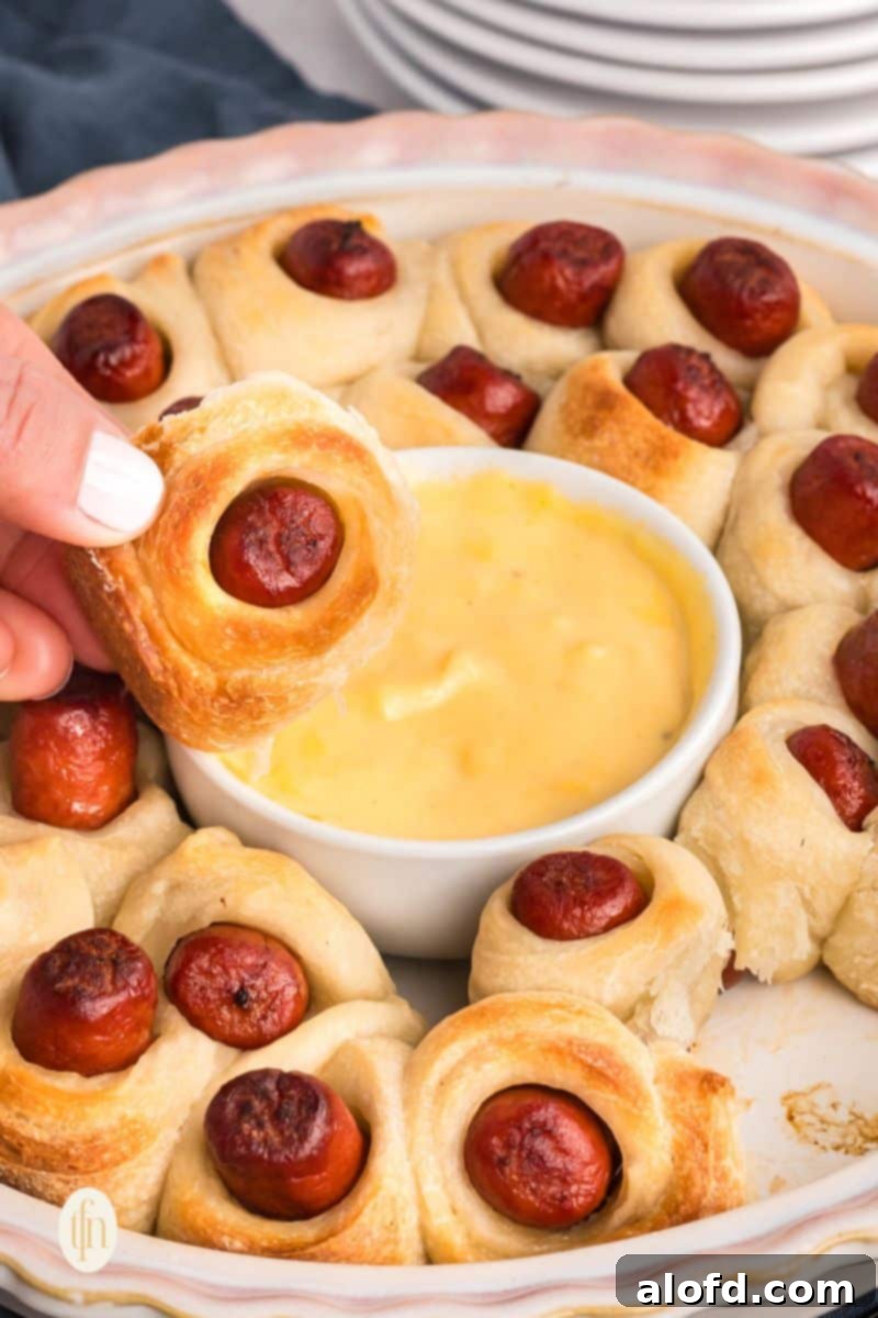 A bowl of sauce in the middle of baked pigs in a blanket.
