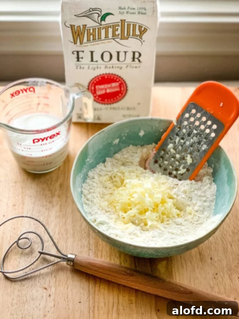 Grating cold butter directly into a bowl of self-rising flour, a key step for flaky drop biscuits.