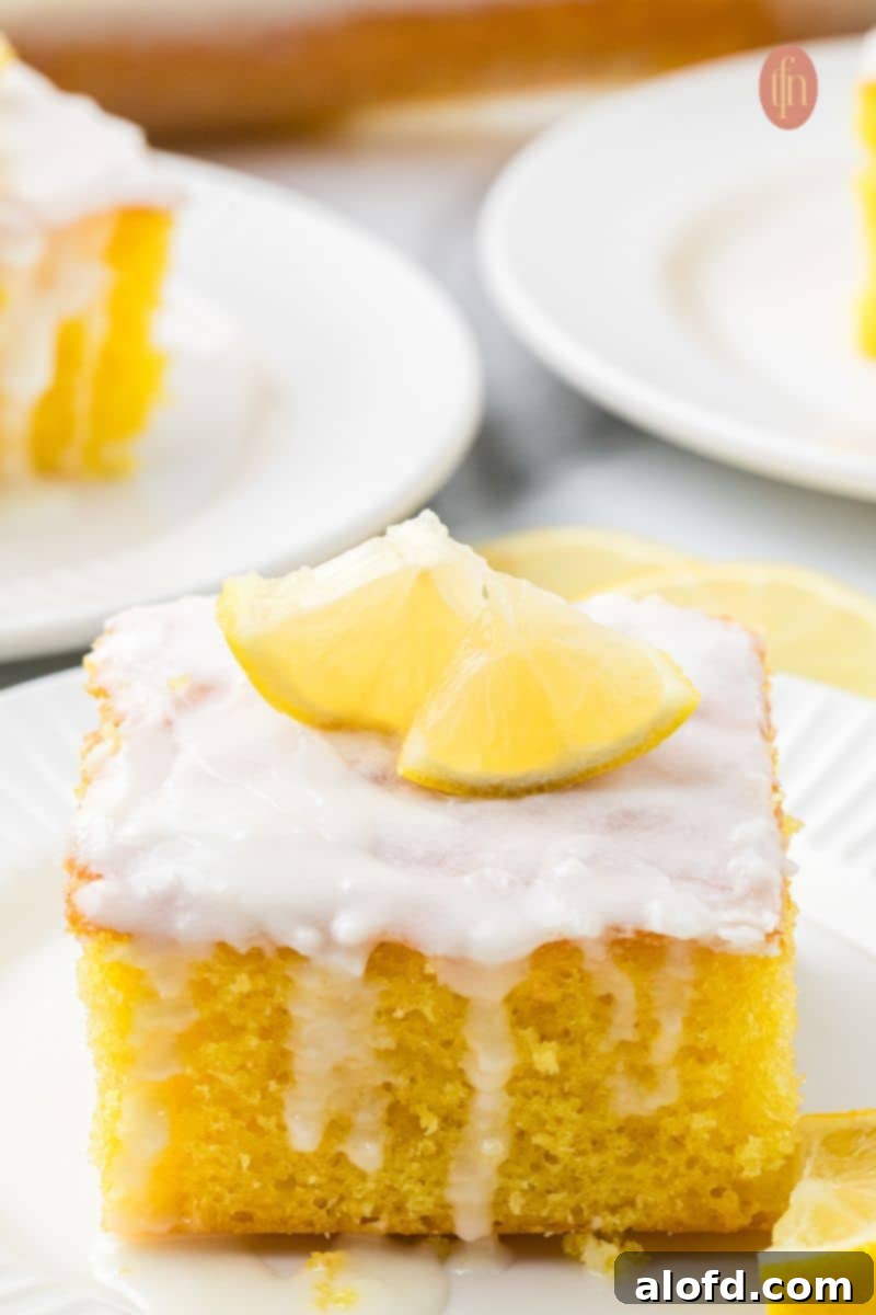 A slice of cake with white glaze and slice of lemon on top.