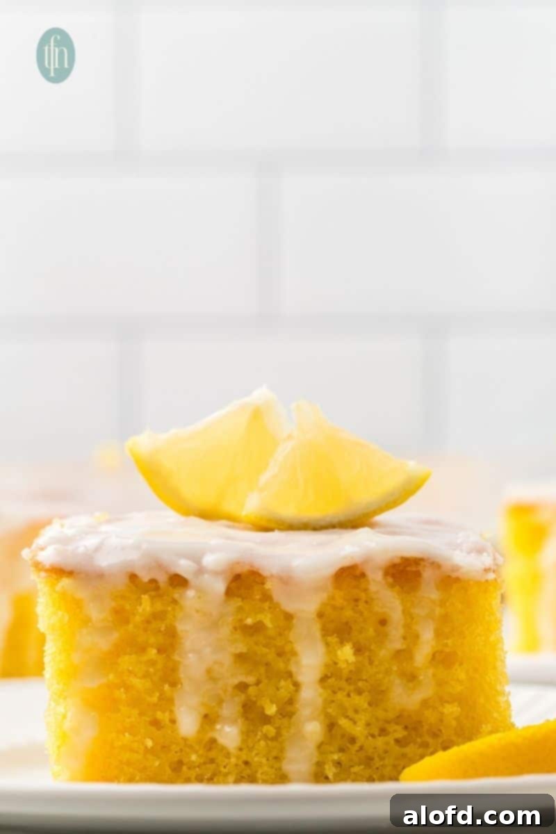 A slice of cake with white glaze and slice of lemon on top.