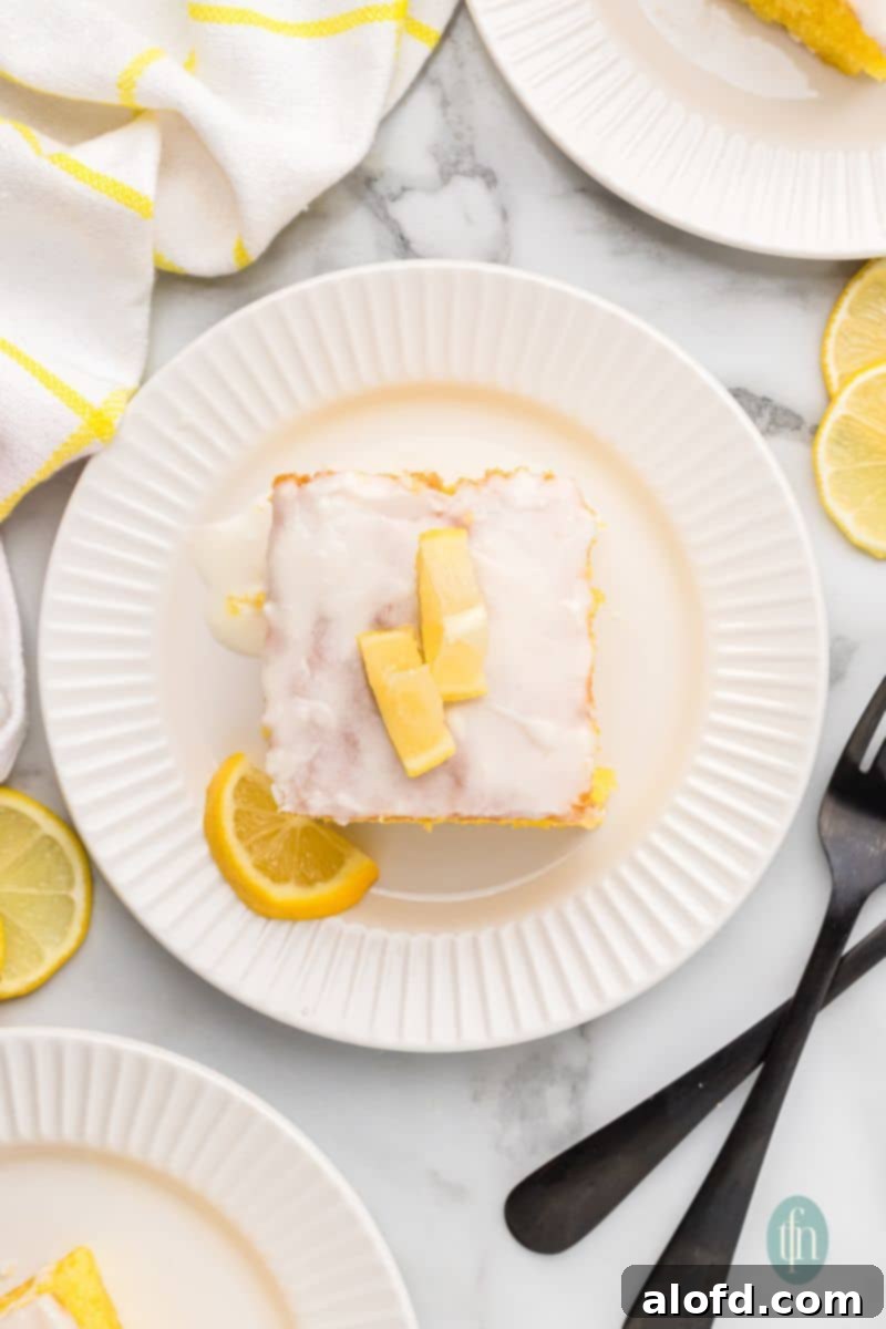 A slice of cake with white glaze and slice of lemon on top.