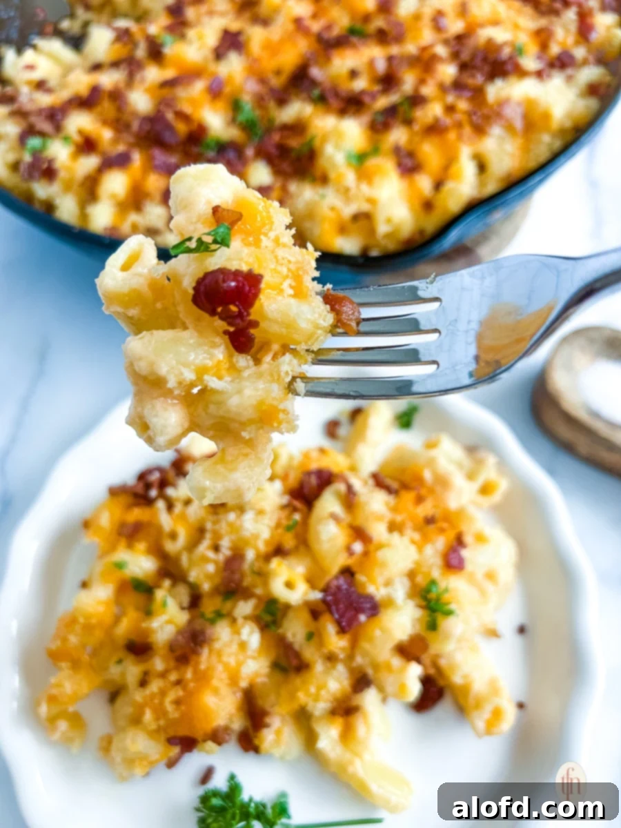 Comforting February Dinners: 20+ Recipes 5 A close-up shot of a fork lifting a perfect bite of smoked mac and cheese, featuring visible bacon bits, positioned above a plated serving. A rustic skillet containing more of the mac and cheese casserole is blurred in the background.