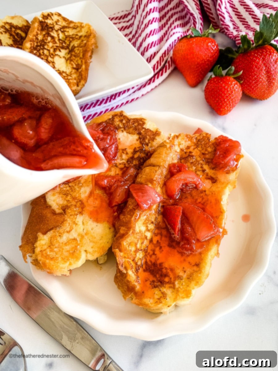 A hand pouring vibrant strawberry syrup over beautifully plated strawberry French toast, ready to be enjoyed.
