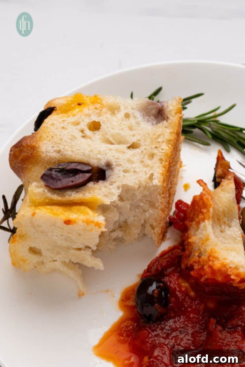 A slice of sourdough focaccia with a dollop of sauce on a white plate, ready to be enjoyed.