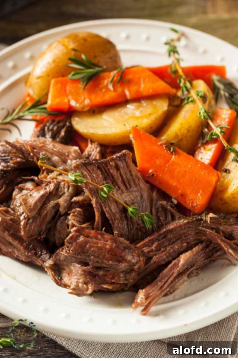 plate of slow cooked chuck roast with carrots and potatoes, a comforting crock pot beef recipe.