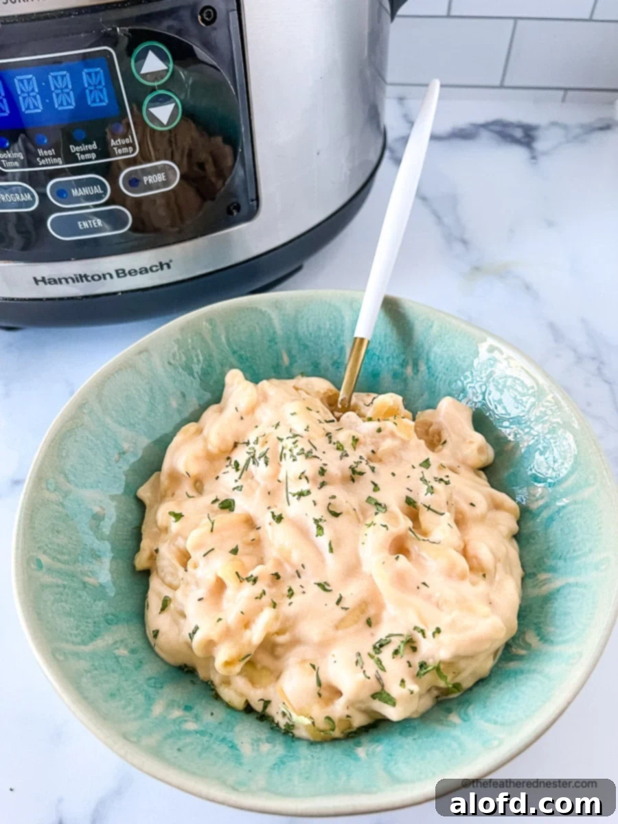 Mac and Cheese with a spoon on a green bowl and a Crock Pot at the back, illustrating a delicious slow cooker pasta recipe.