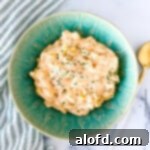 square photo of slow cooker mac and cheese on a green bowl and a spoon at the side, highlighting its creamy texture.