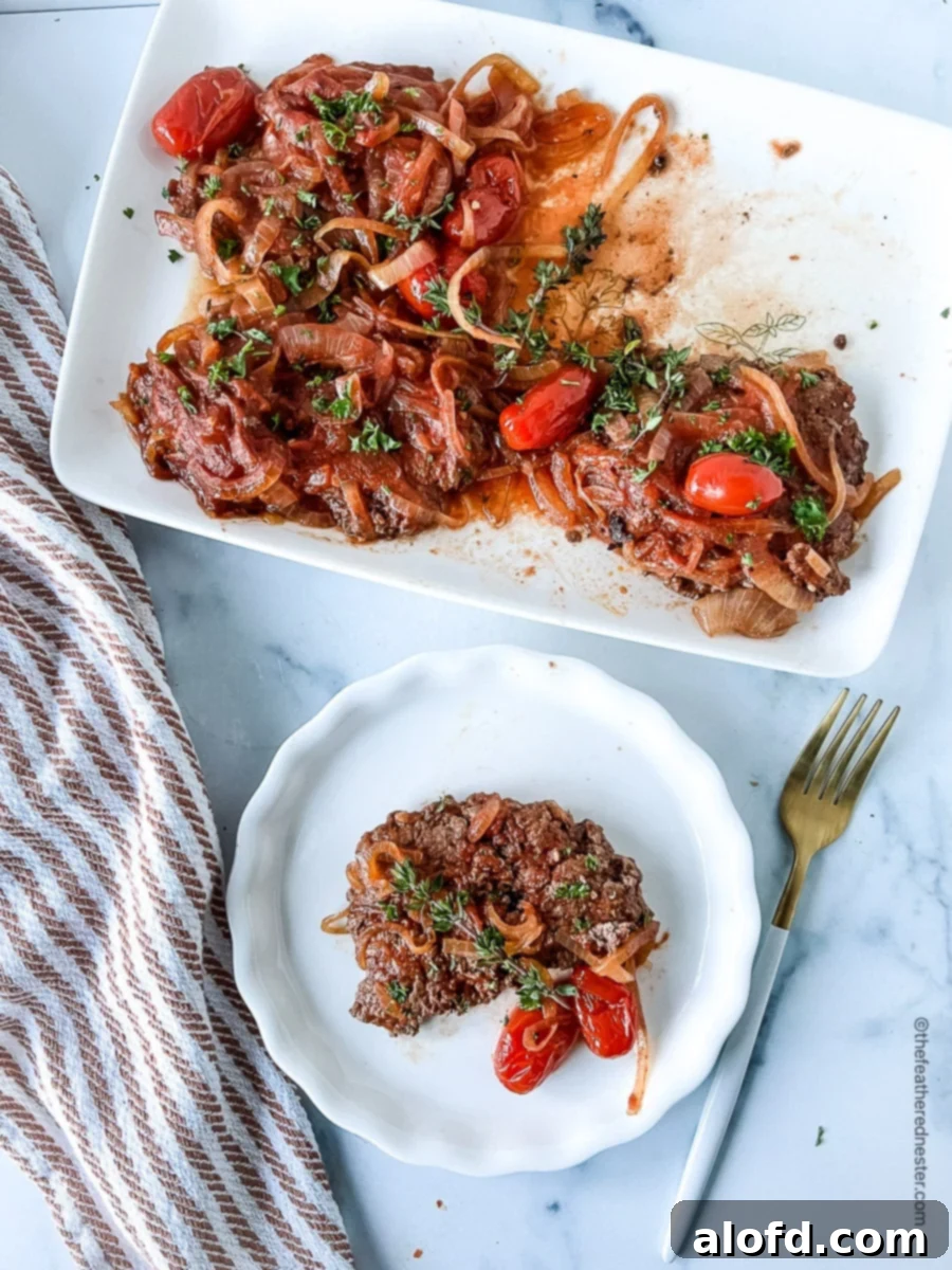 platter of Swiss steak with onions and tomatoes, and a plated serving in front of it, showcasing a tender crock pot beef recipe.