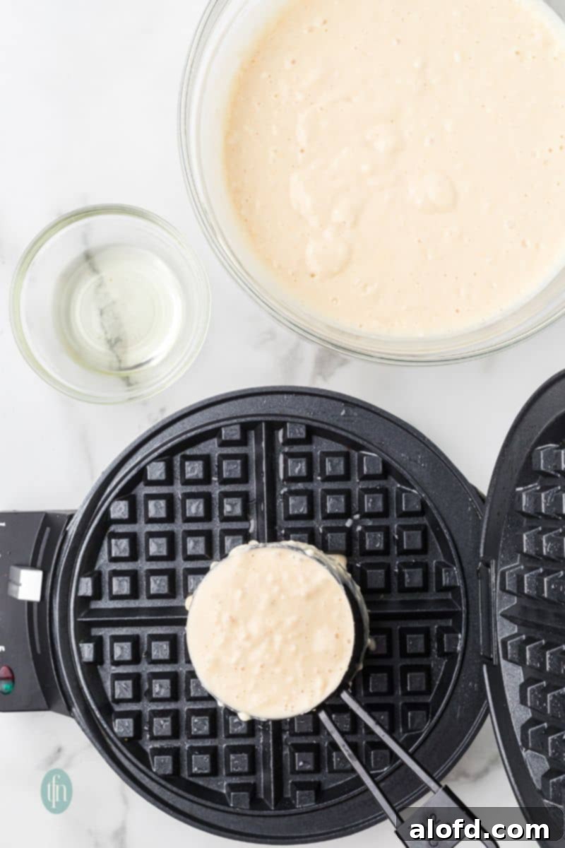 Fluffy Golden Bisquick Waffles 11 A waffle maker with a cup of batter.