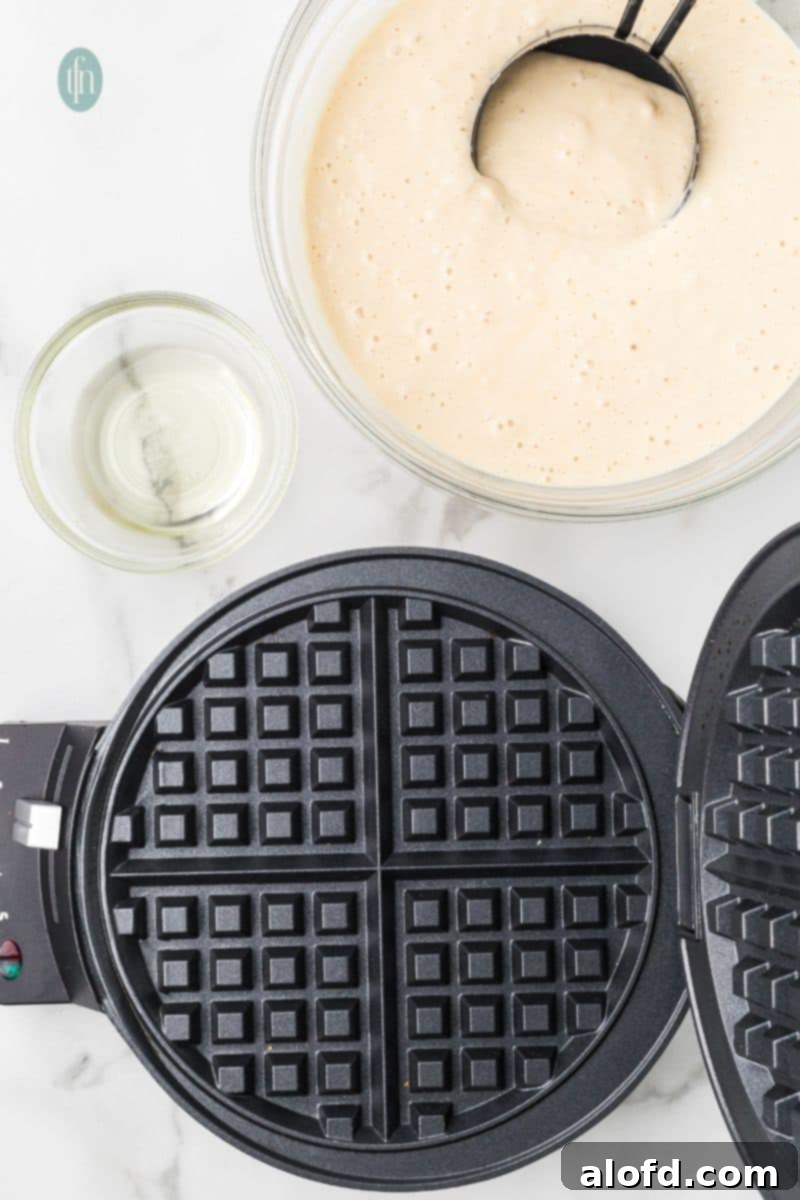 Fluffy Golden Bisquick Waffles 6 A waffle maker and a bowl of batter mixture.