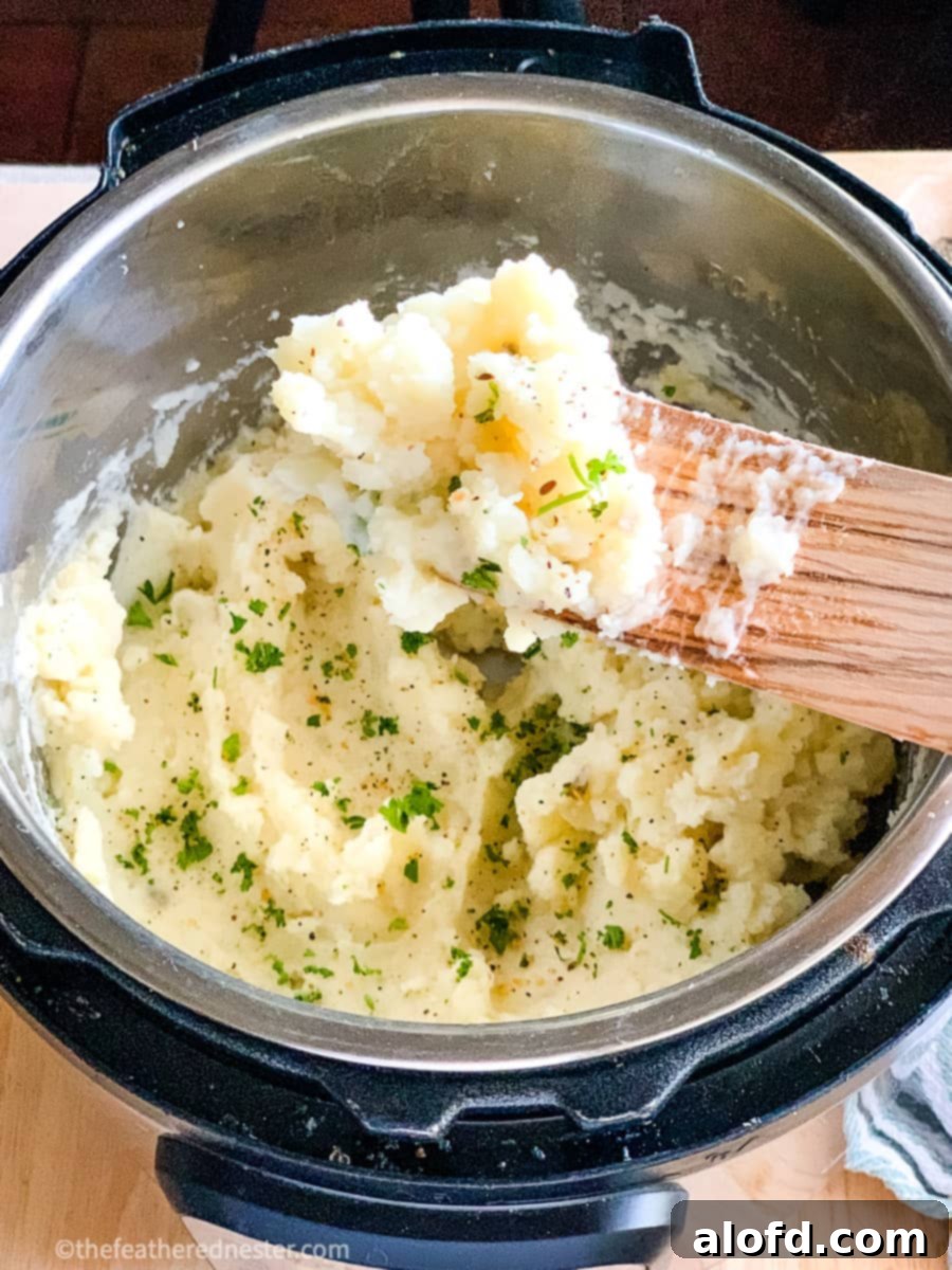 Foolproof Instant Pot No-Drain Mash 9 Close up of Instant Pot Mashed Potatoes on a wooden spoon held above the pressure cooker.