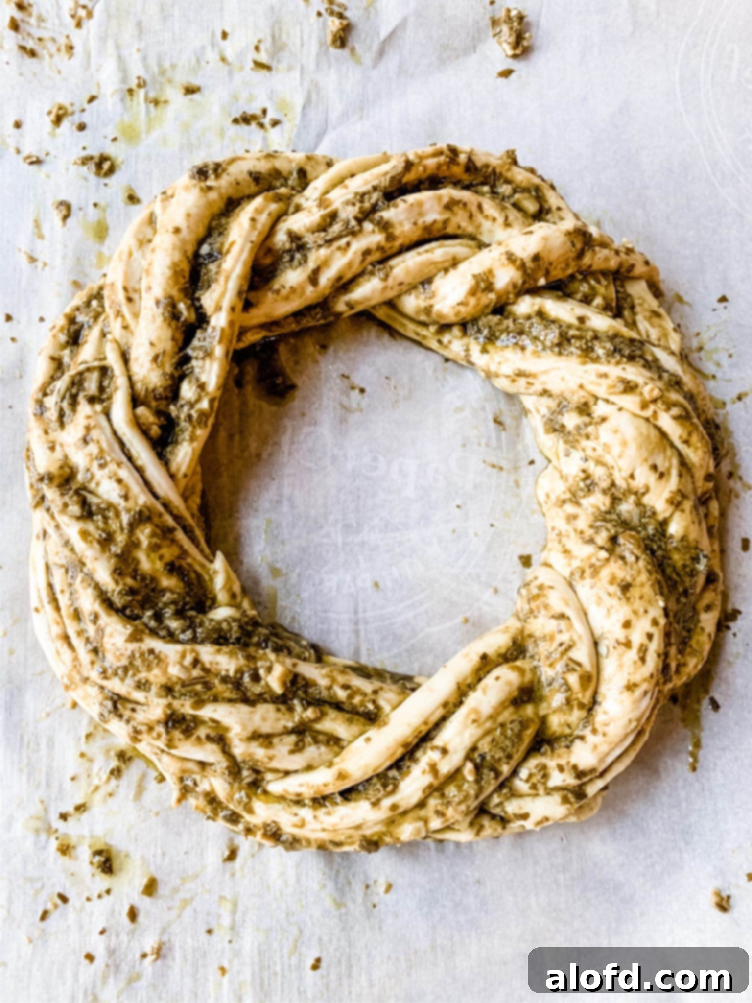 Pesto bread wreath on parchment paper, ready for baking.
