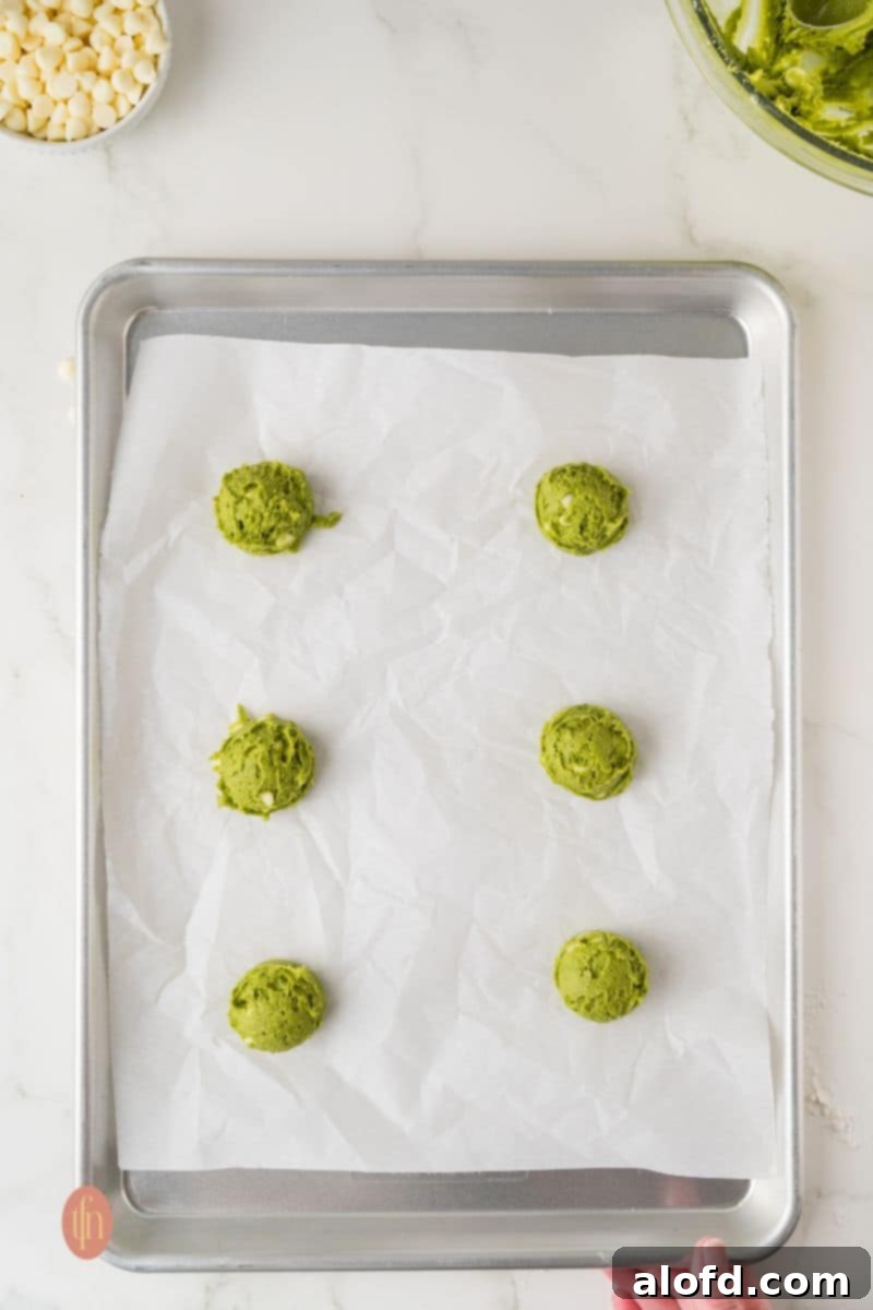 Vibrant Matcha White Chocolate Cookies 11 Six evenly spaced balls of green cookie dough on a parchment-lined baking pan, ready for the oven.