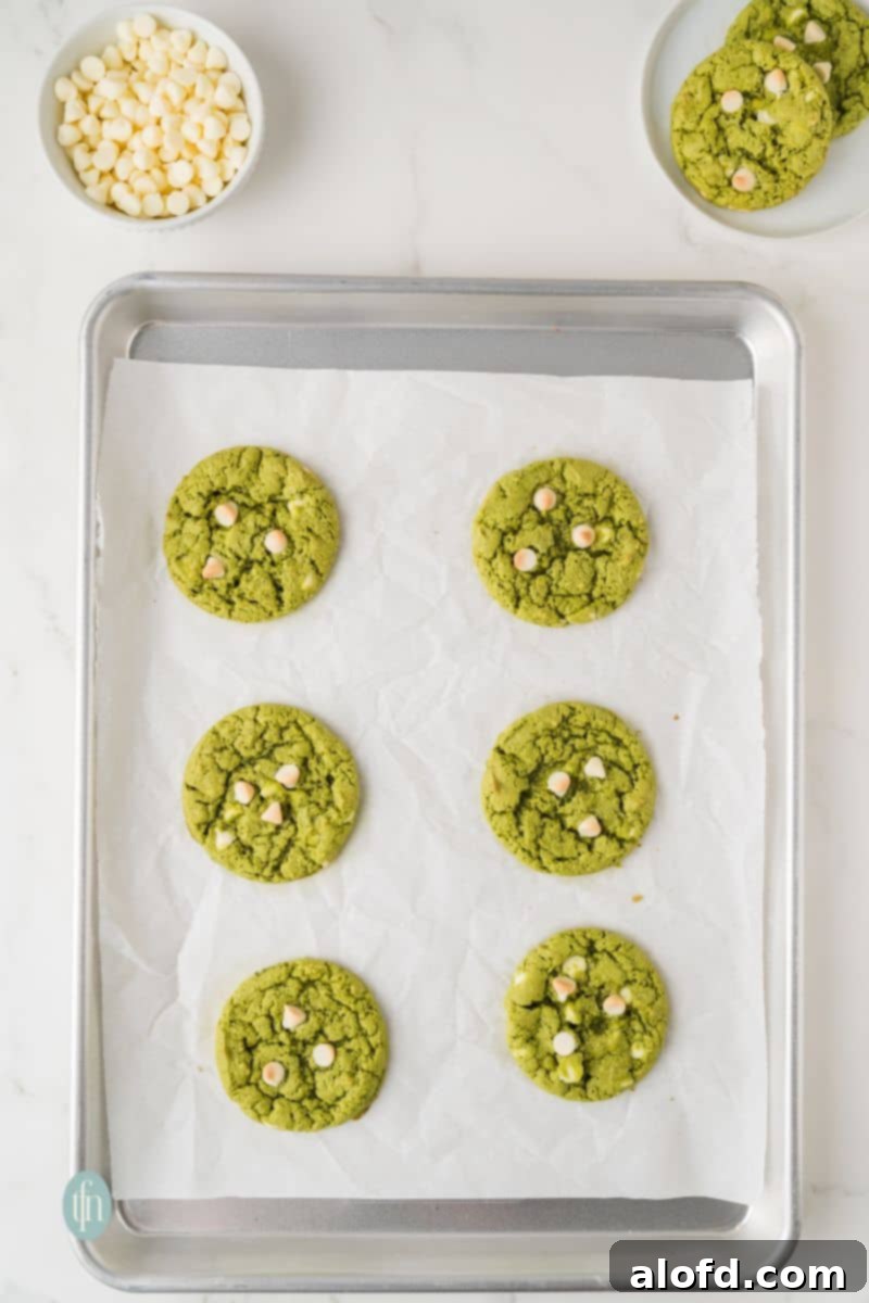 Vibrant Matcha White Chocolate Cookies 12 Freshly baked green matcha white chocolate cookies on a baking pan, still warm from the oven.