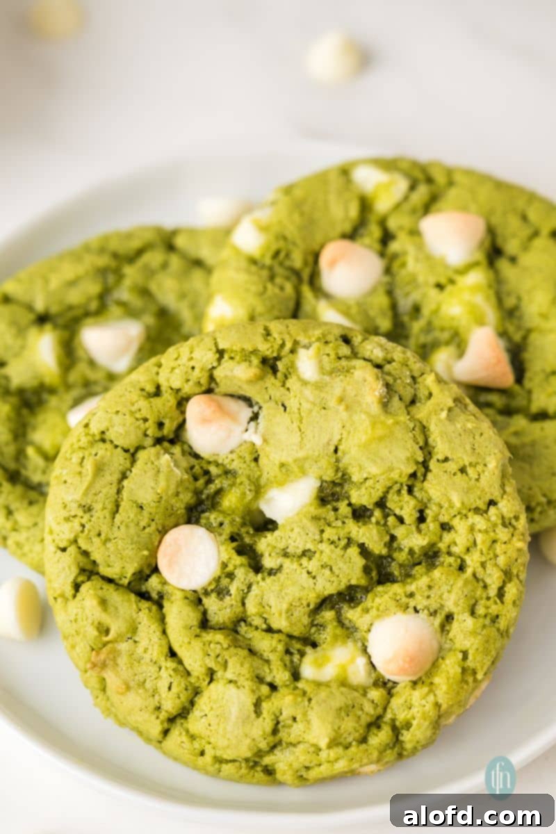 Vibrant Matcha White Chocolate Cookies 3 A close-up shot of several green matcha white chocolate cookies on a plate, highlighting their vivid color and chewy texture.