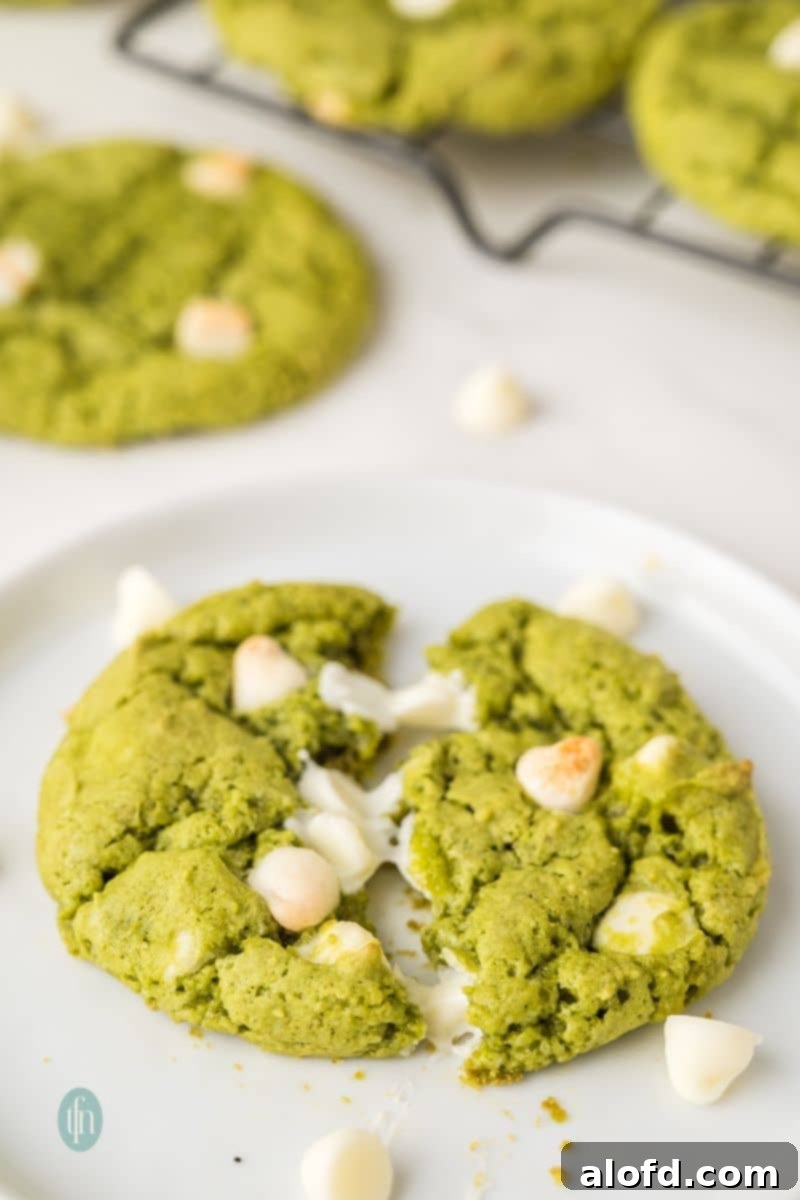 Vibrant Matcha White Chocolate Cookies 4 A single green matcha white chocolate cookie placed on a rustic white plate, emphasizing its texture and appealing color.