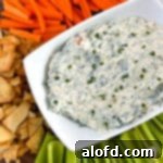 A rectangular serving bowl filled with creamy Knorr spinach dip, elegantly presented on a round wooden board alongside an assortment of crackers and fresh vegetables.