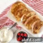 A pristine white platter generously adorned with golden slices of French toast, accompanied by a small bowl of fresh mixed berries and a dollop of whipped cream, all set on a charming red and white striped napkin.