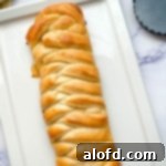 A beautifully golden lemon braided bread loaf, elegantly presented on a pristine white platter.