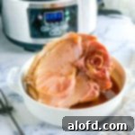 A glistening ham cooked with Coke, with the Crock Pot subtly visible in the background, hinting at its effortless preparation.