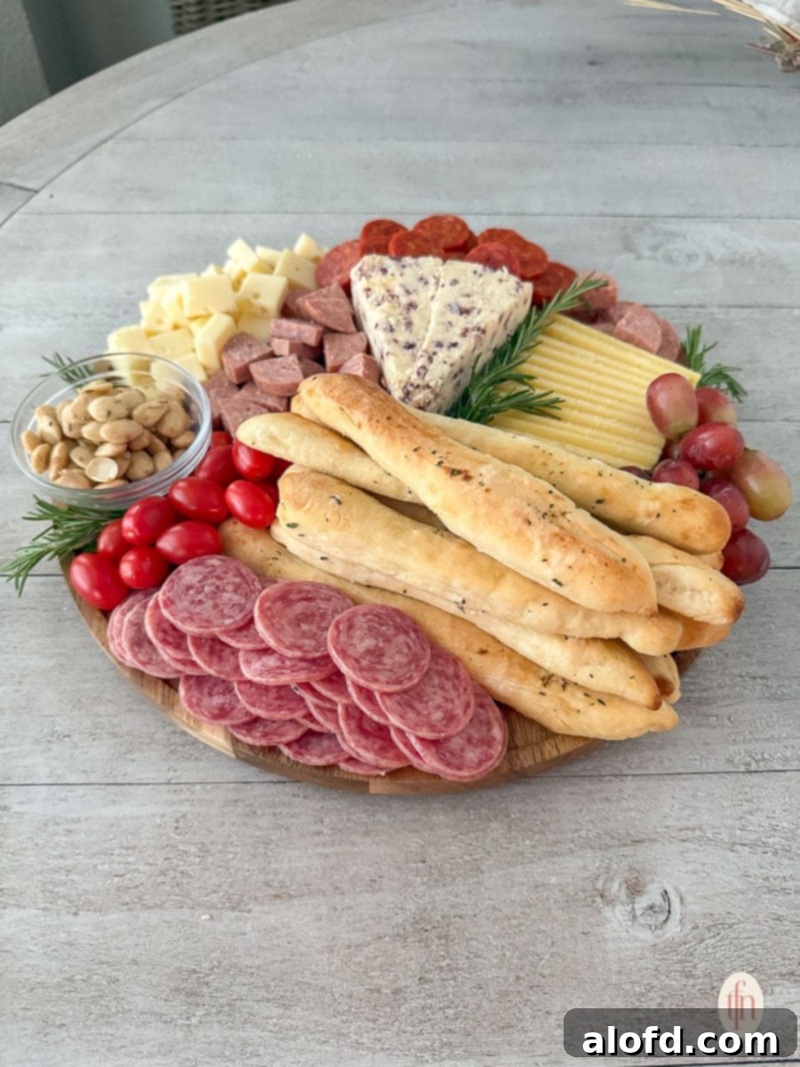 A beautifully arranged round charcuterie board featuring an assortment of bread, cured meats, cherry tomatoes, fresh fruits, and gourmet cheeses.