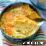 A spoonful of Instant Pot cheesy potatoes suspended above the remaining casserole, highlighting its creamy texture.