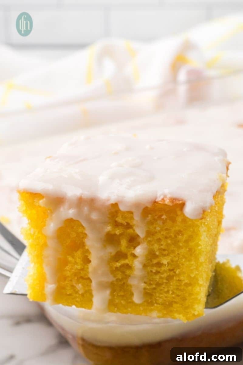 A perfectly baked slice of lemon jello poke cake, generously coated with a delicate white glaze.