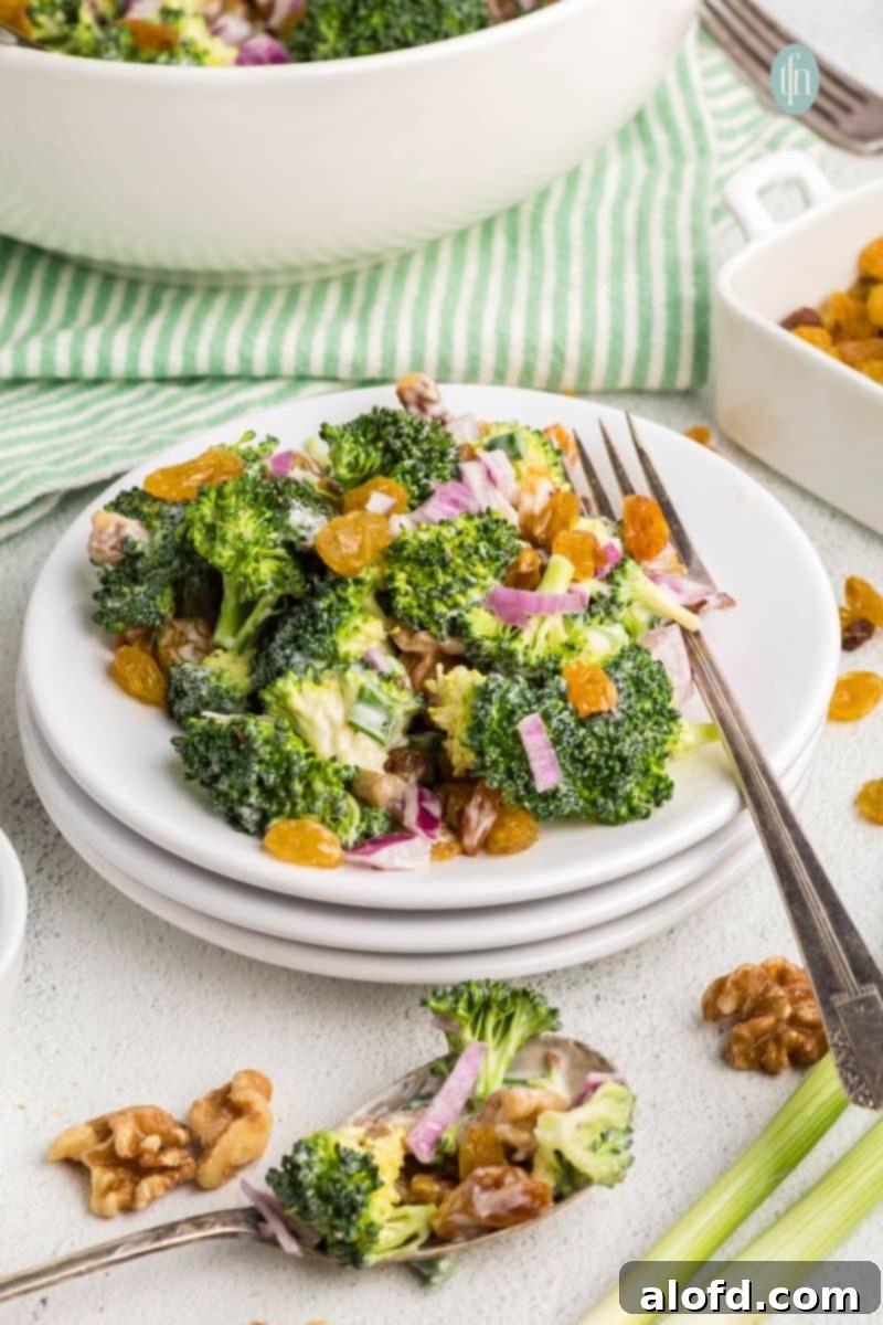 A vibrant bowl of broccoli raisin salad with bacon, ready to be served at a family gathering or picnic. The creamy dressing glistens on the fresh broccoli florets, sweet golden raisins, and crunchy walnuts, while crispy bacon bits add a savory depth. This is the ultimate side dish for any occasion.