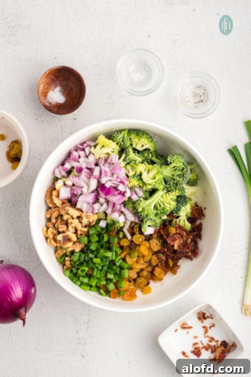 Chopped broccoli florets, red onion, and green onions in a large white mixing bowl, ready for the dressing.
