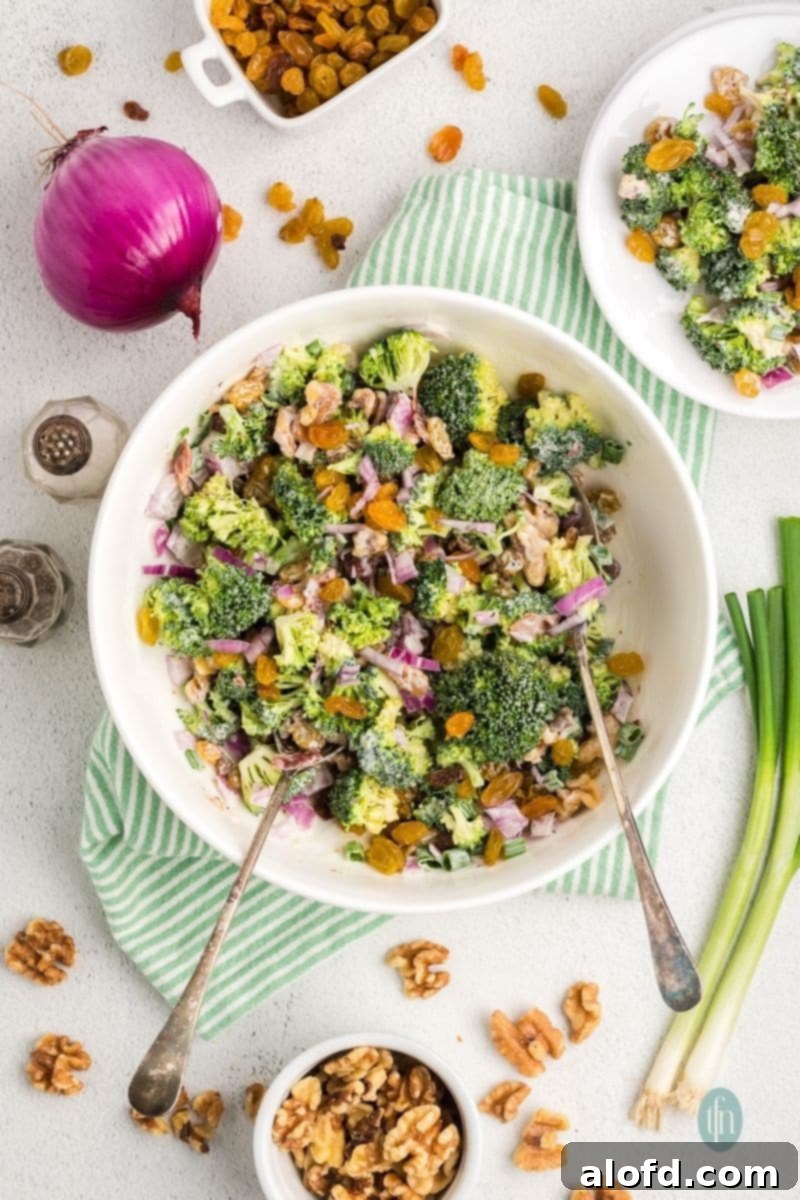 A large white bowl of freshly mixed broccoli raisin salad, ready to be chilled or served.