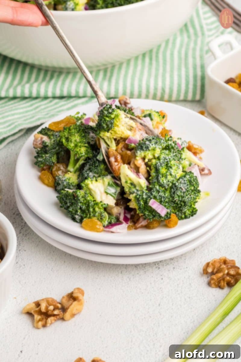 A beautifully presented broccoli raisin salad on a white plate, highlighting its creamy texture and fresh ingredients, with a fork ready to enjoy.