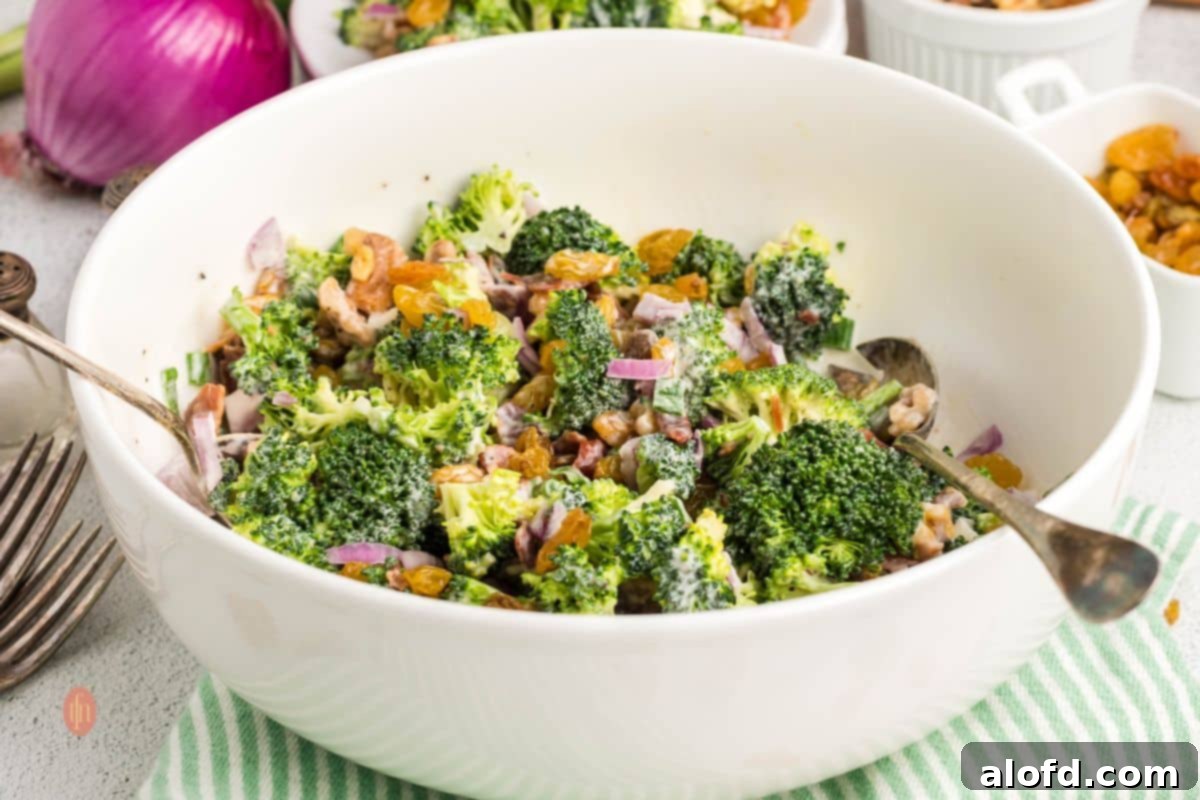A broad shot of a large bowl of fresh broccoli salad with bacon and raisins, garnished and ready for a meal.