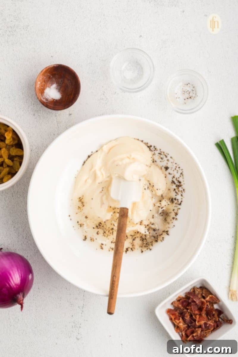 Mayonnaise, vinegar, and sugar being whisked together in a white mixing bowl to create the creamy dressing.