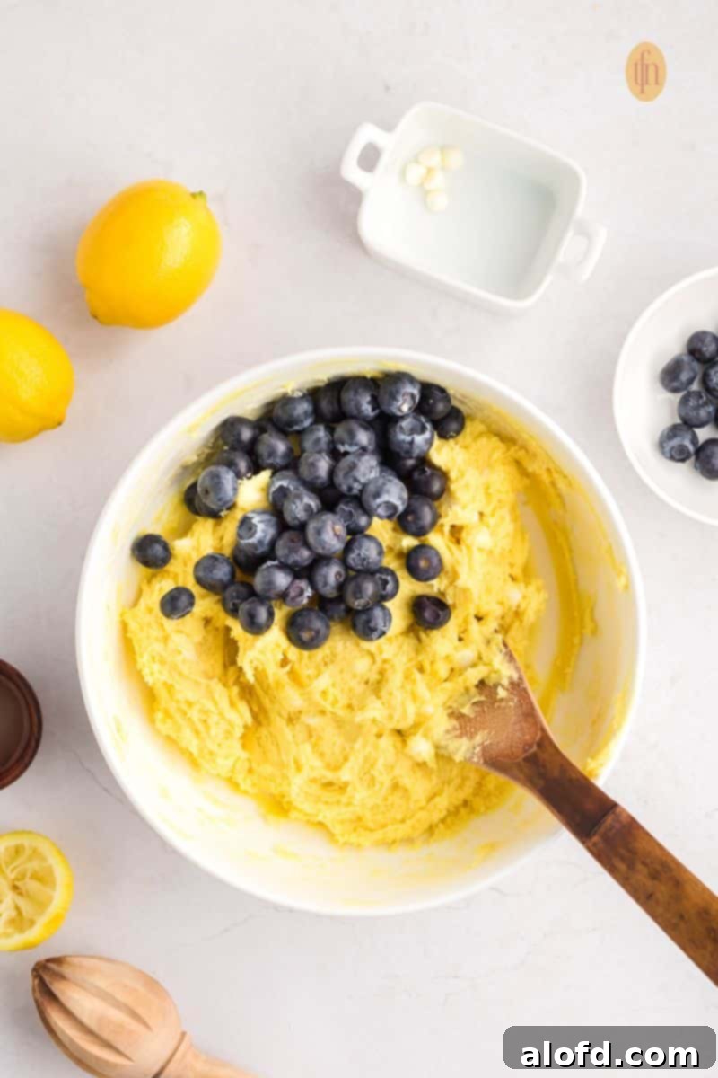 Lemon Blueberry Bliss Bites 12 Blueberries being added to the cookie dough in a white bowl.