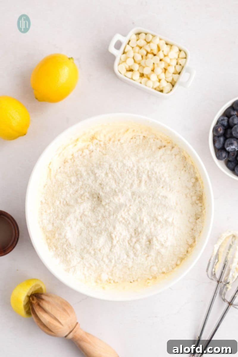 Lemon Blueberry Bliss Bites 9 Cake mix being added to the wet batter in a white bowl.