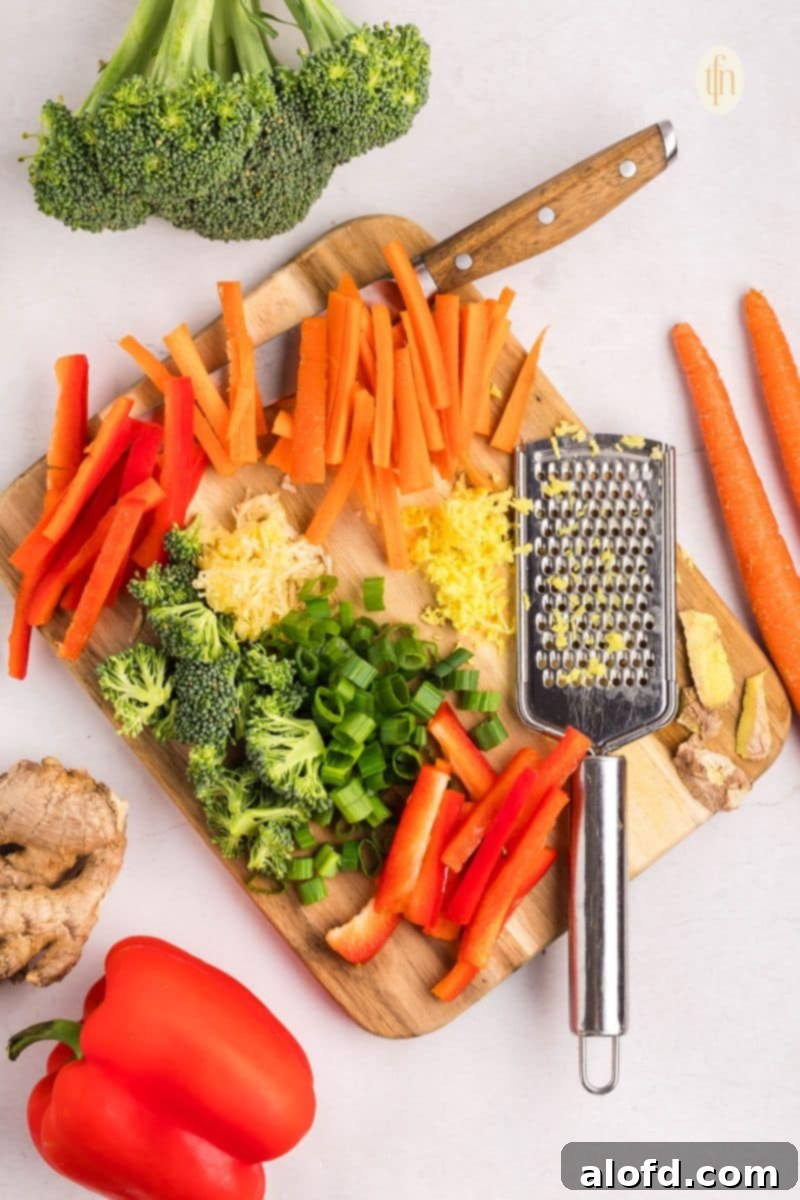 Freshly chopped broccoli, carrots, and red bell pepper on a cutting board, ready for cooking.