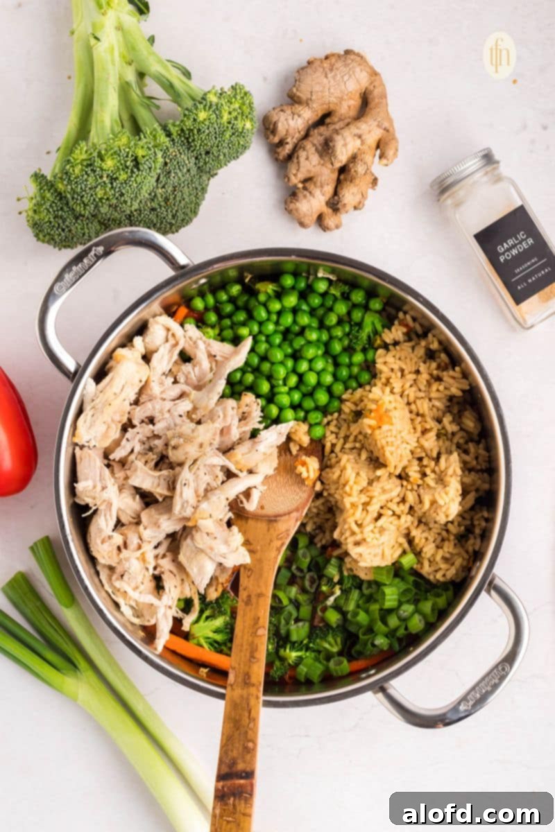 Ingredients for chicken and rice bowl, including chicken, rice, vegetables, and sauce, laid out in a pan before mixing.