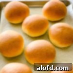 Homemade burger buns on a baking sheet.