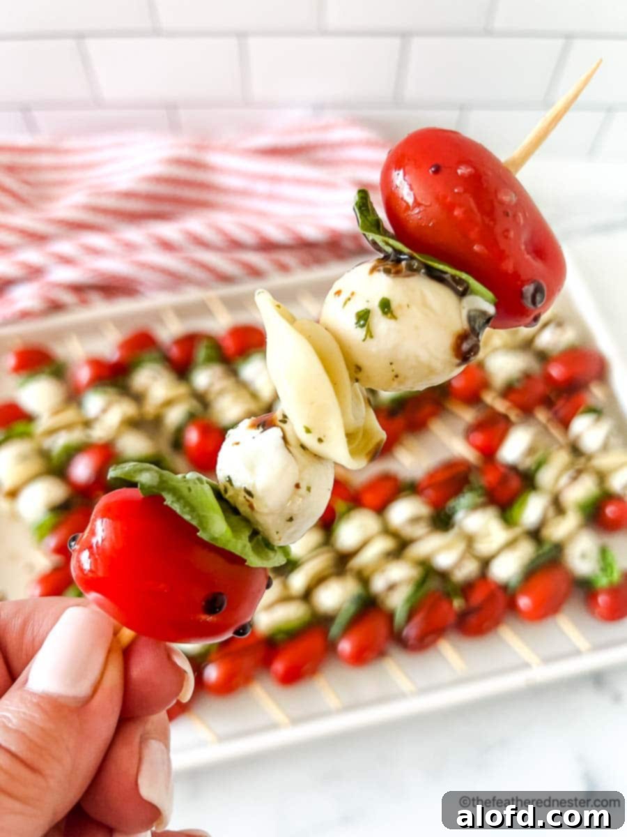 a closeup of a caprese tortellini appetizer with a tray of caprese skewers with balsamic glaze and a red and white napkin in the background. A perfect starter for your Memorial Day gathering.