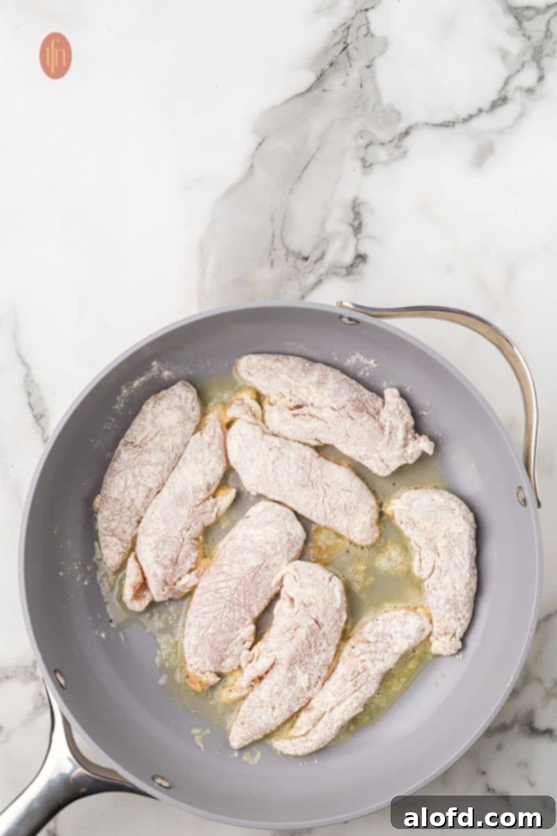 Zesty Lemon Chicken Orzo Pasta 12 Flour-coated chicken pieces searing beautifully in a hot frying pan, showcasing the golden crust beginning to form.