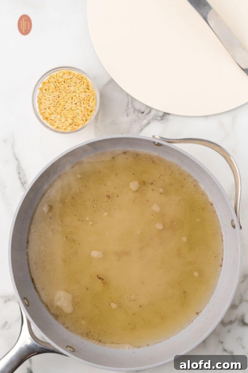 Zesty Lemon Chicken Orzo Pasta 14 A pan with simmering chicken broth next to a bowl of dry orzo pasta, illustrating the next step of cooking the orzo.