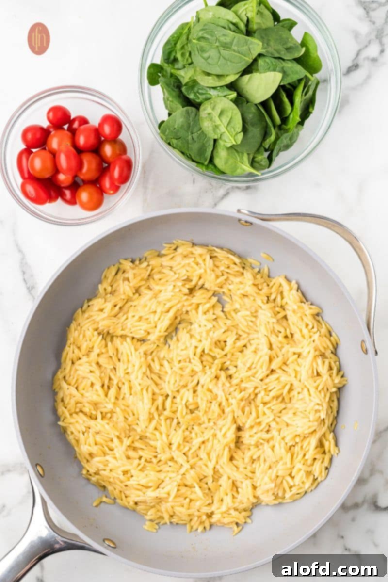 Zesty Lemon Chicken Orzo Pasta 16 Cooked orzo in a pan, with separate bowls of fresh grape tomatoes and baby spinach or kale, indicating they are ready to be stirred in.