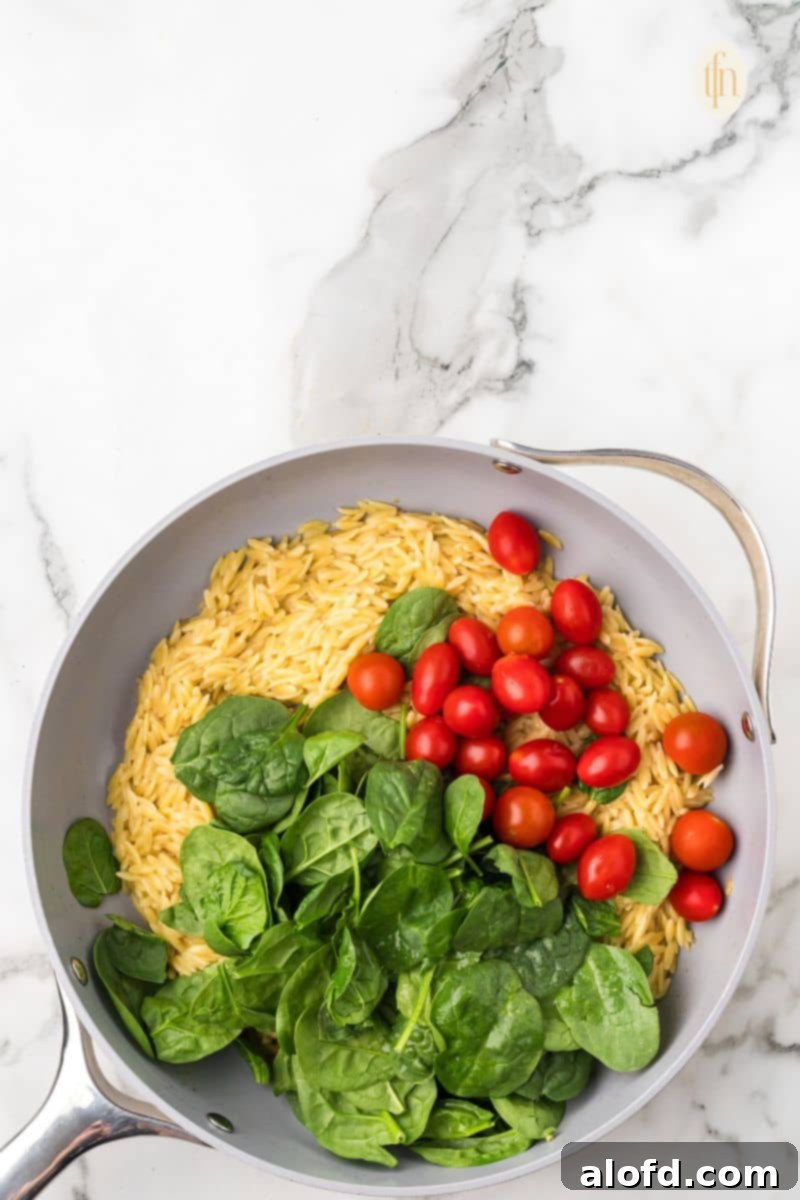 Zesty Lemon Chicken Orzo Pasta 18 A pan of orzo pasta thoroughly mixed with vibrant grape tomatoes and perfectly wilted green leafy vegetables, showcasing the colorful and appetizing medley.