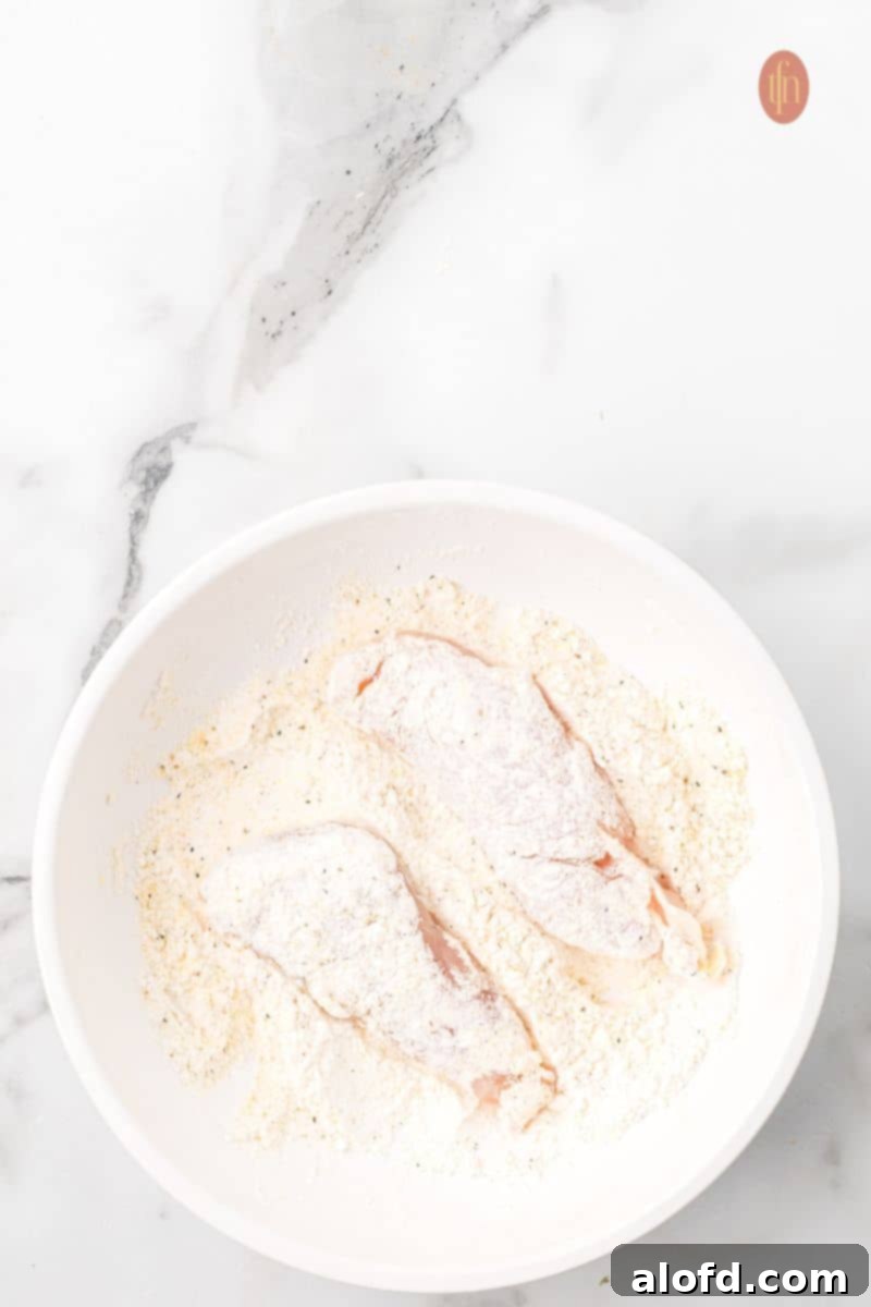 Zesty Lemon Chicken Orzo Pasta 10 Another view of two chicken pieces being coated in a dry flour mixture, emphasizing the meticulous process of achieving an even, thorough coating.